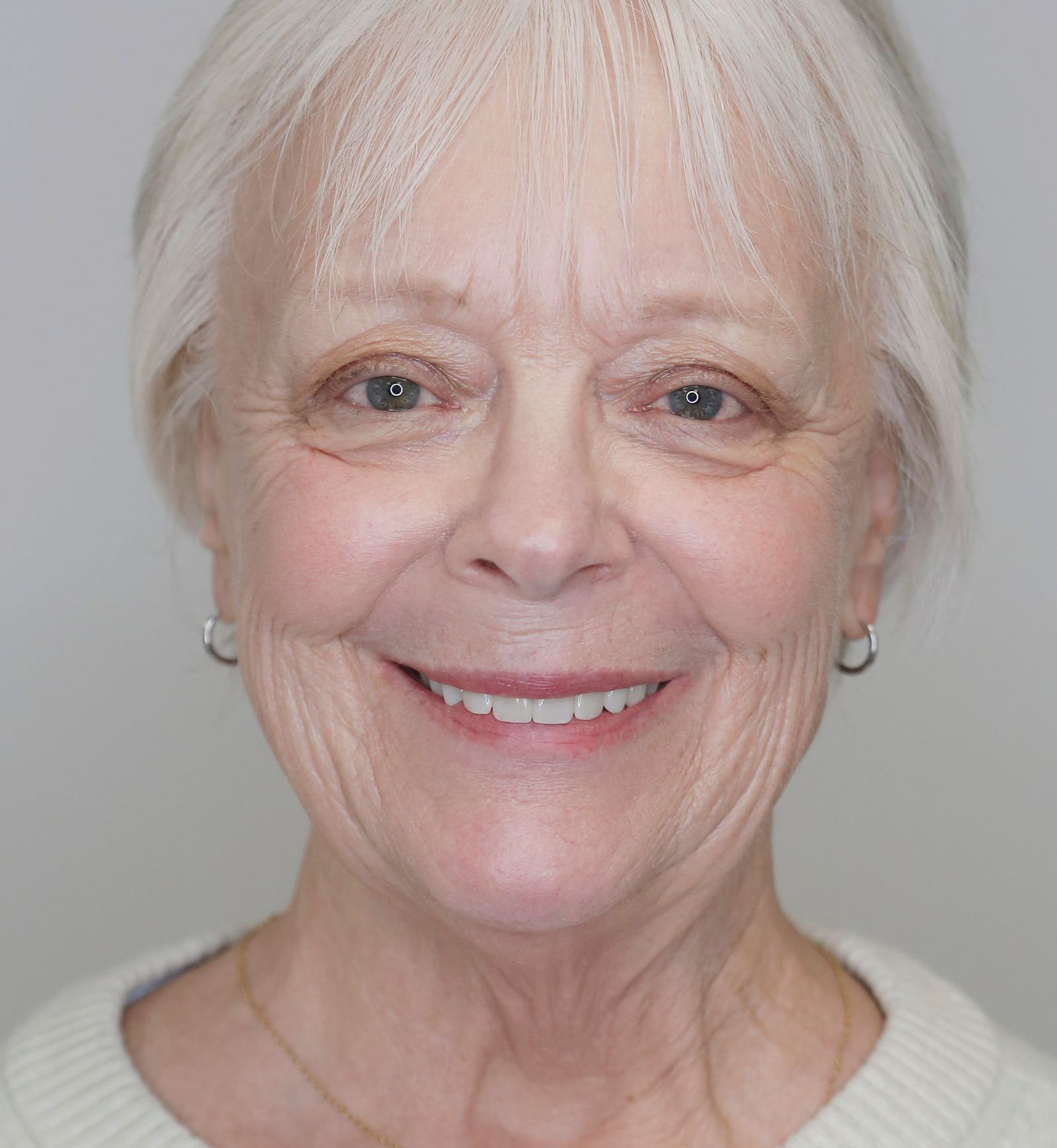 Smiling woman with short white hair against a gray background