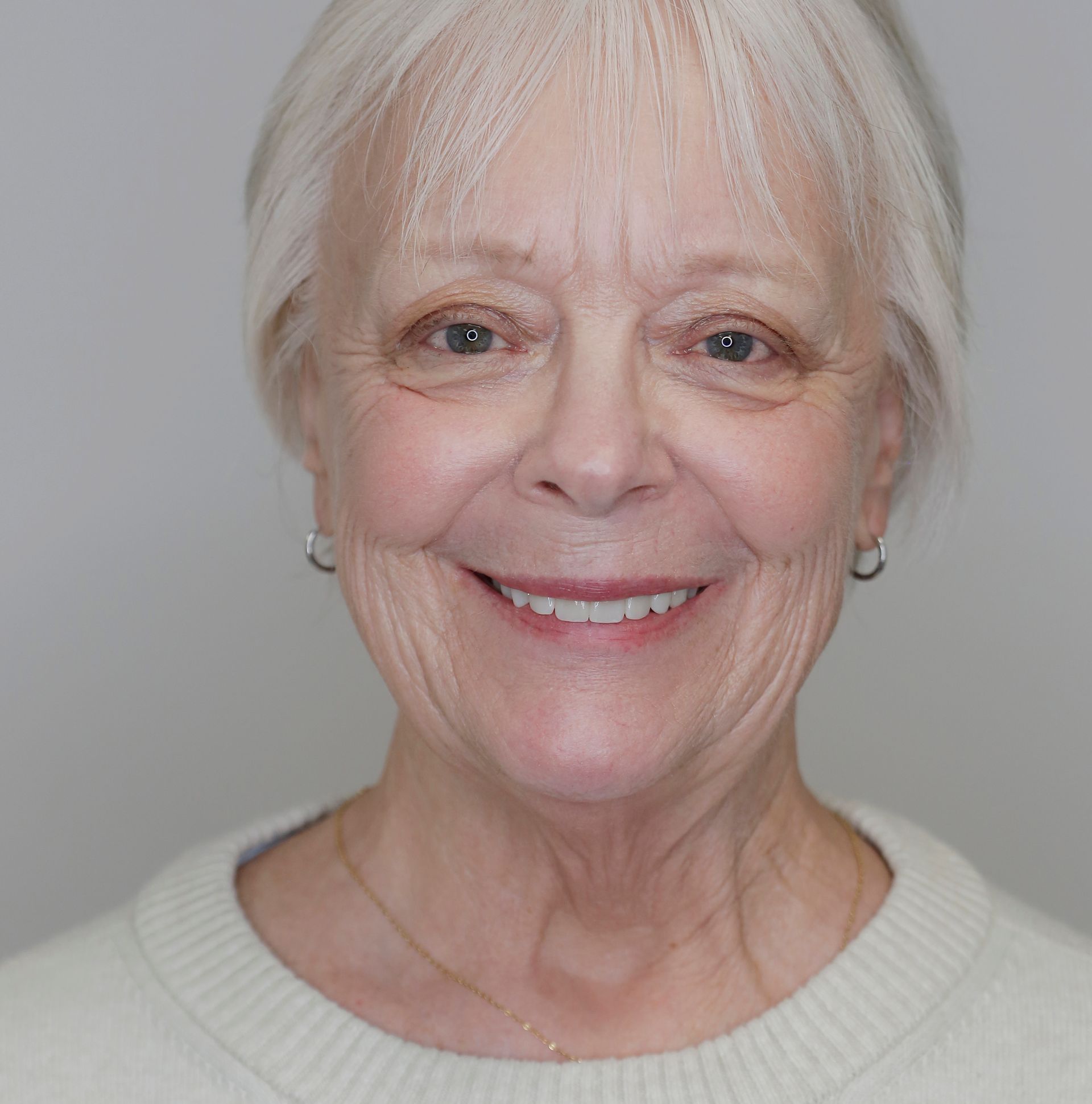 Smiling woman with short white hair against a plain gray background