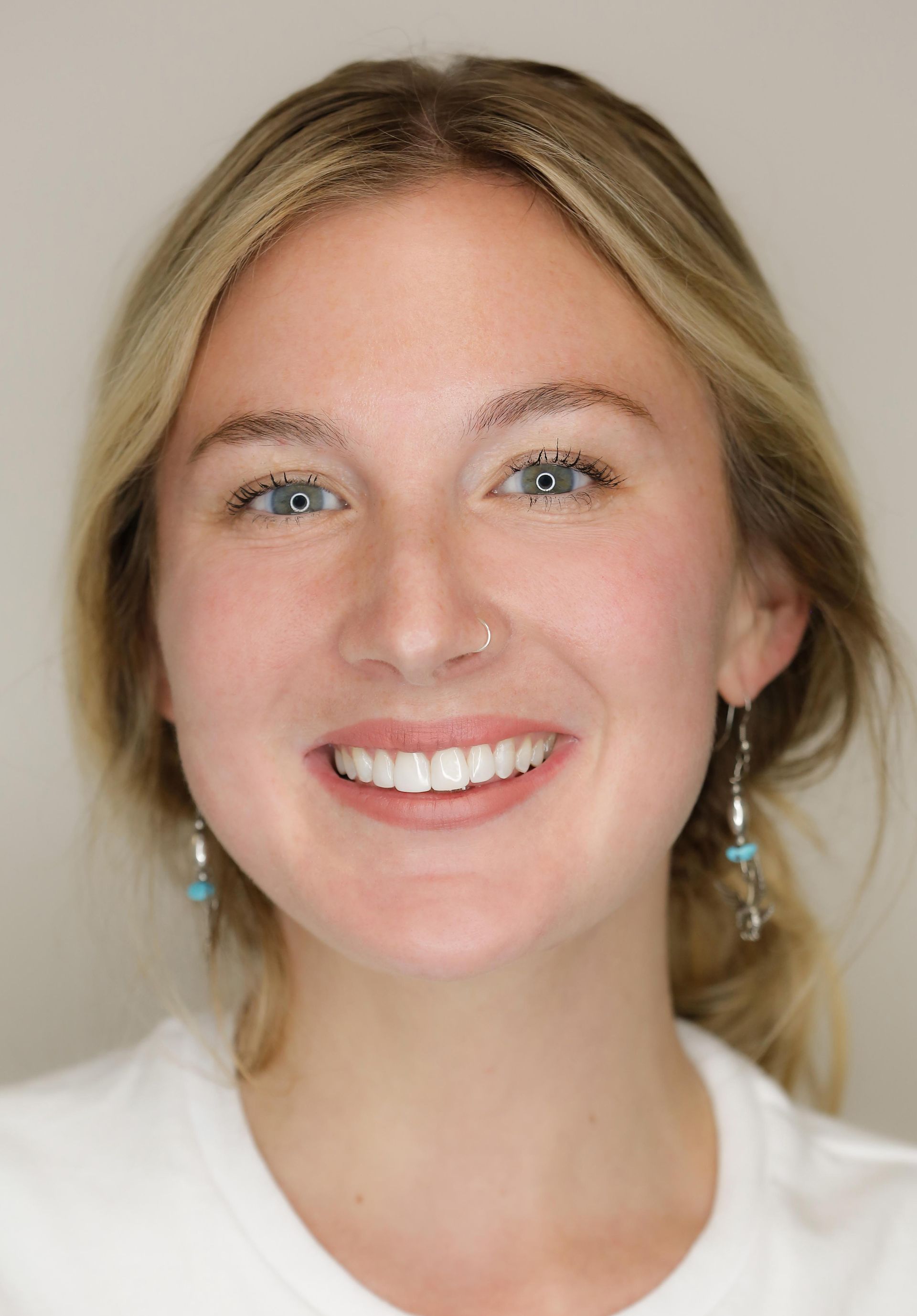 Smiling woman with blonde hair and dangling earrings against a neutral background