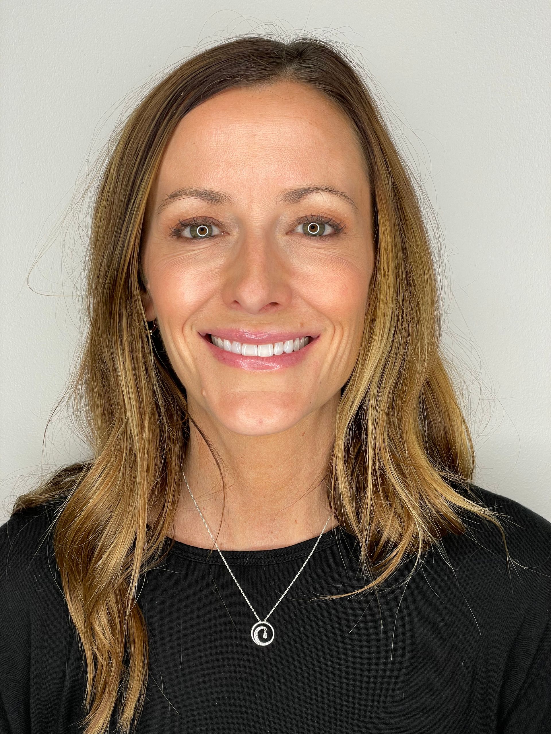 A woman wearing a black shirt and a necklace is smiling for the camera.