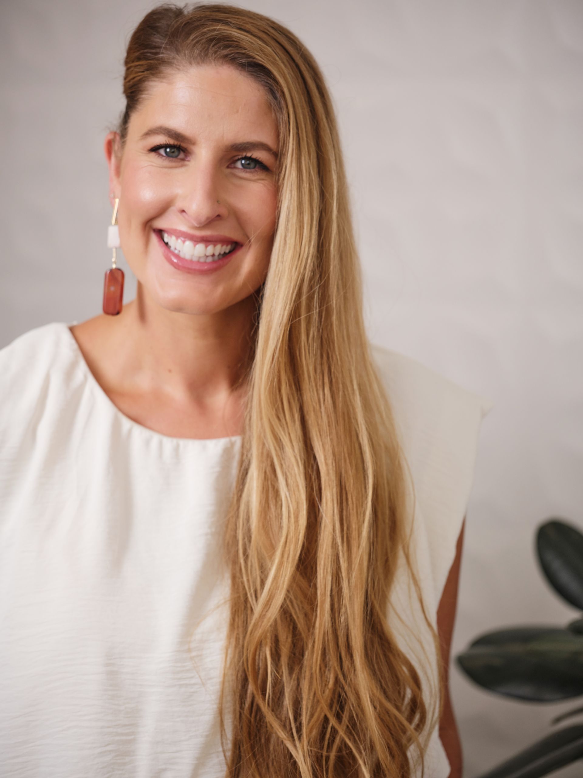 Smiling woman with long blonde hair in a white blouse against a neutral background