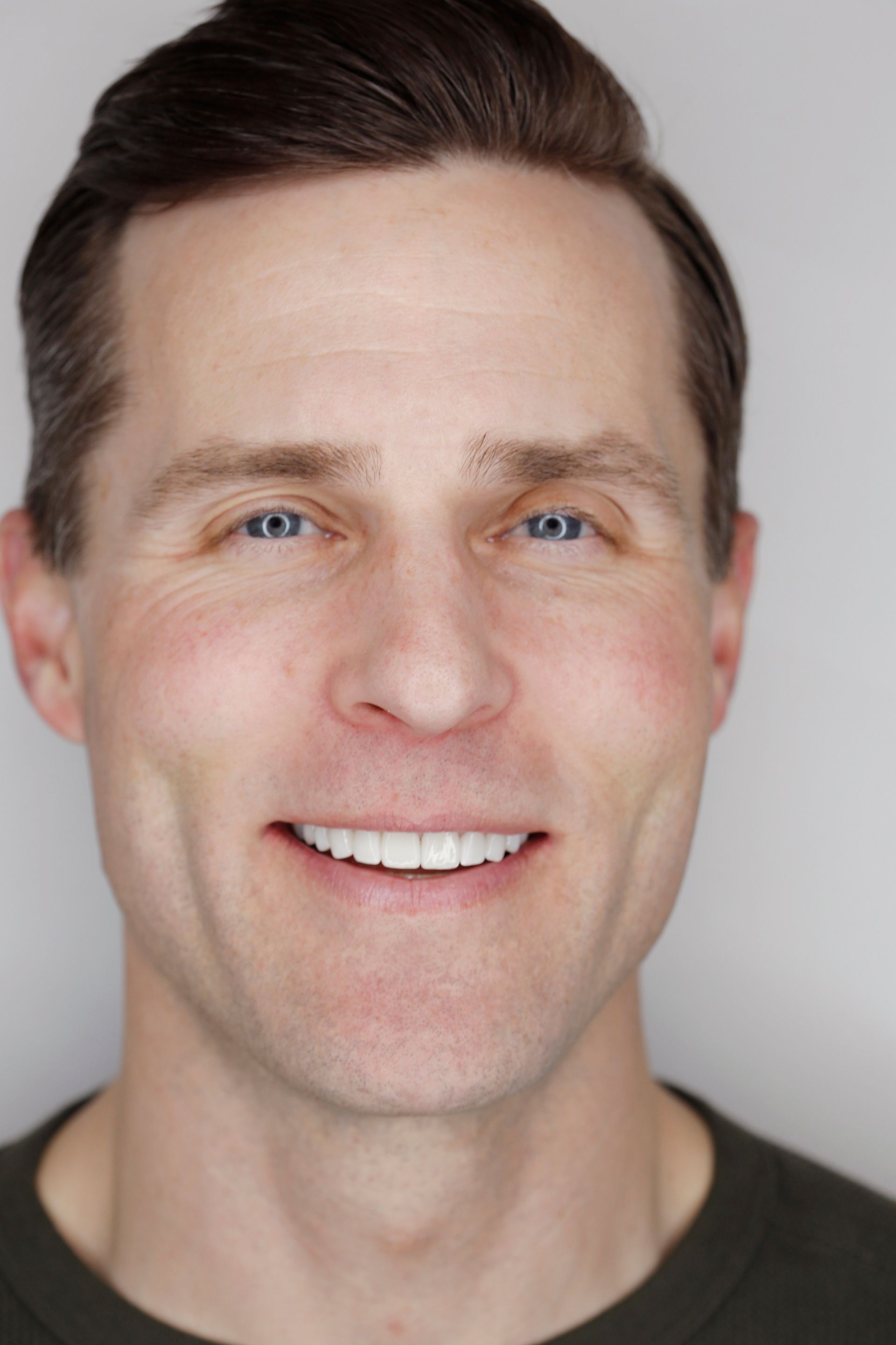 Headshot of a smiling man with short brown hair against a light gray background