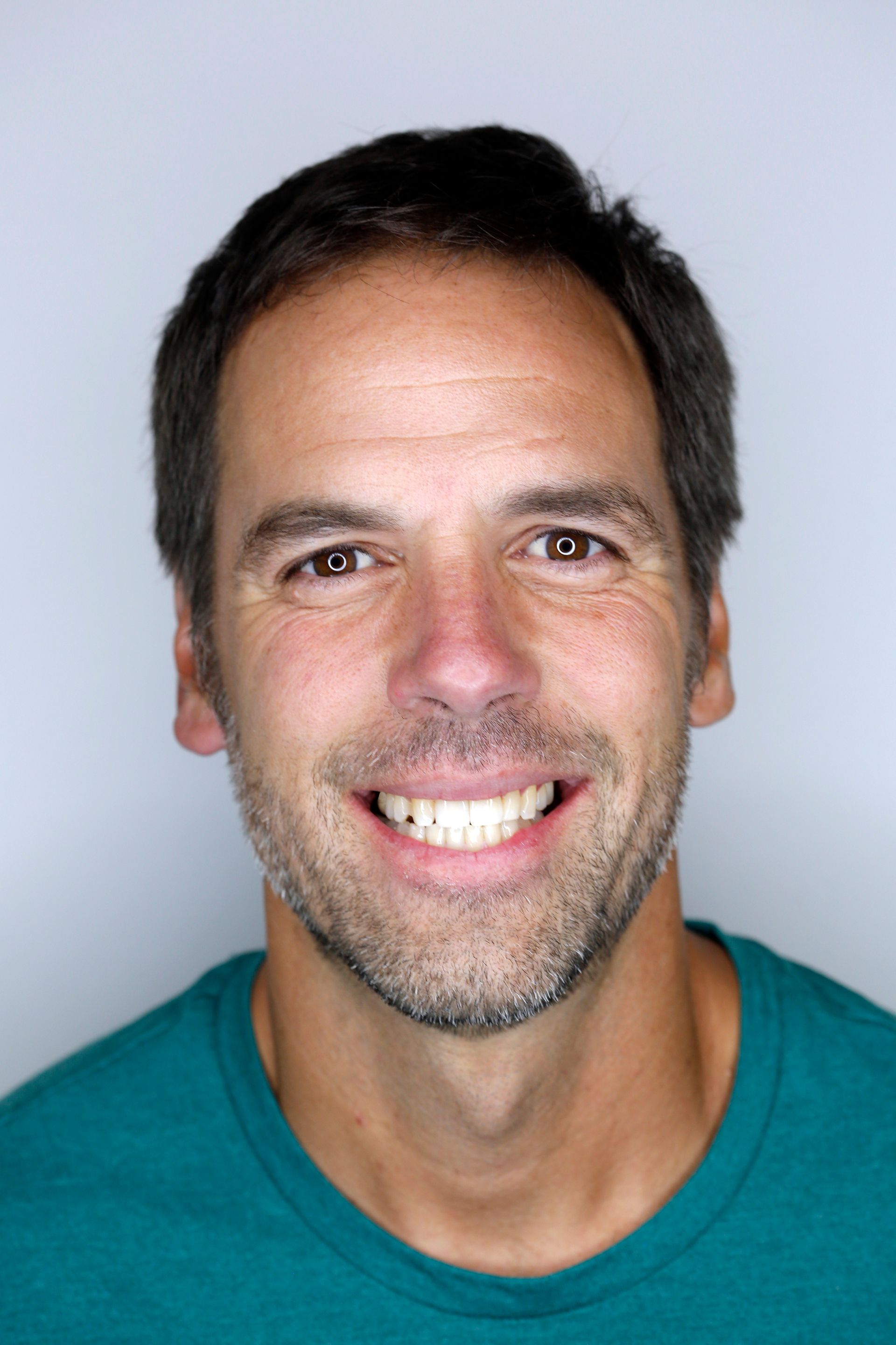 A man with a beard is smiling for the camera while wearing a blue shirt.