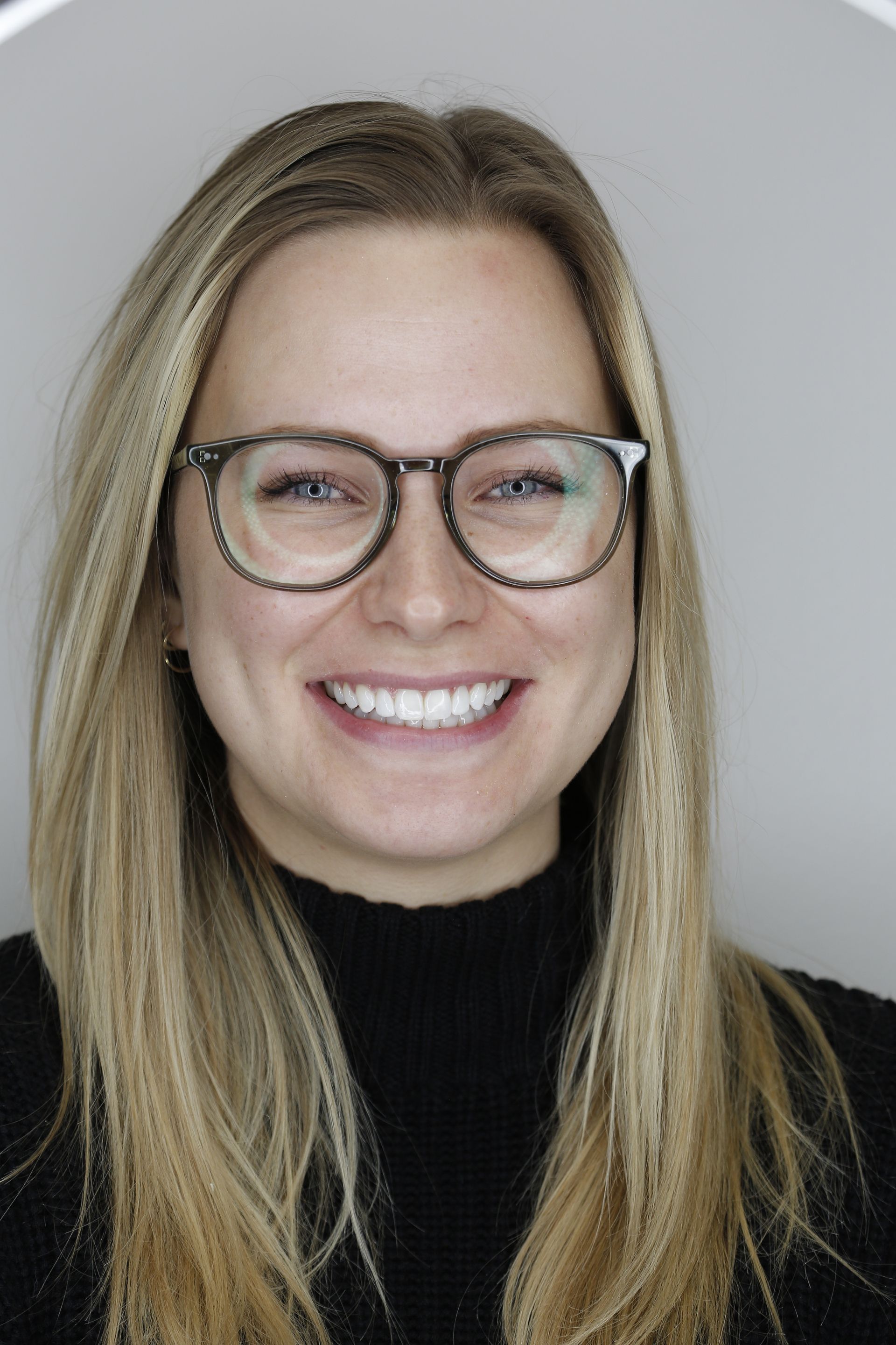 A woman wearing glasses and a black turtleneck is smiling.