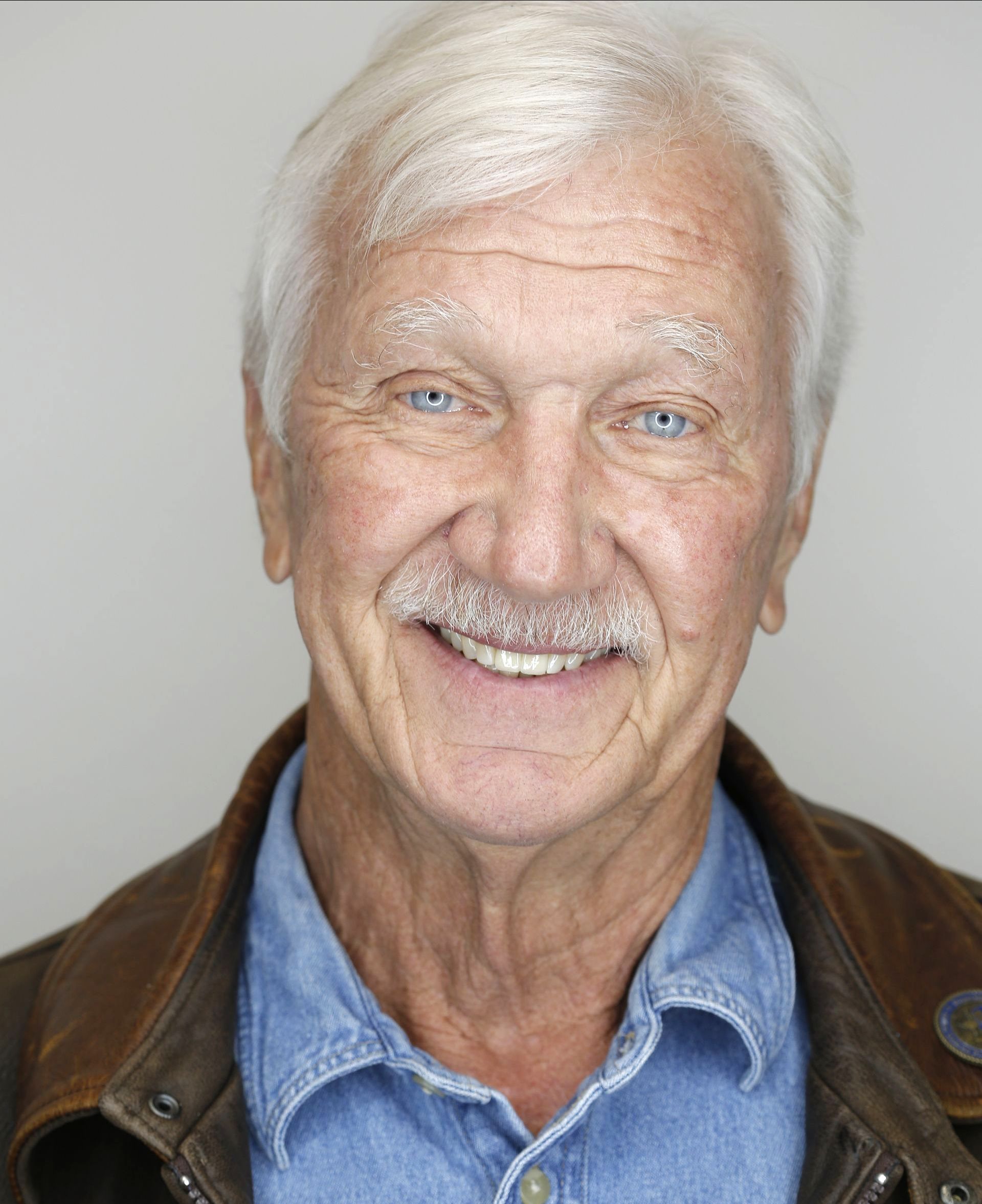 A man with white hair and a mustache is smiling for the camera
