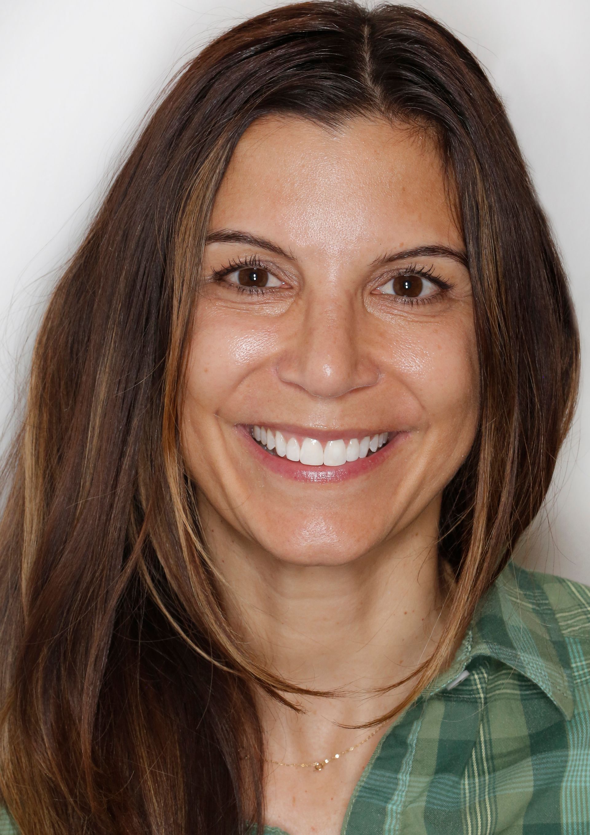 Smiling woman with long brown hair in a green plaid shirt against a light background