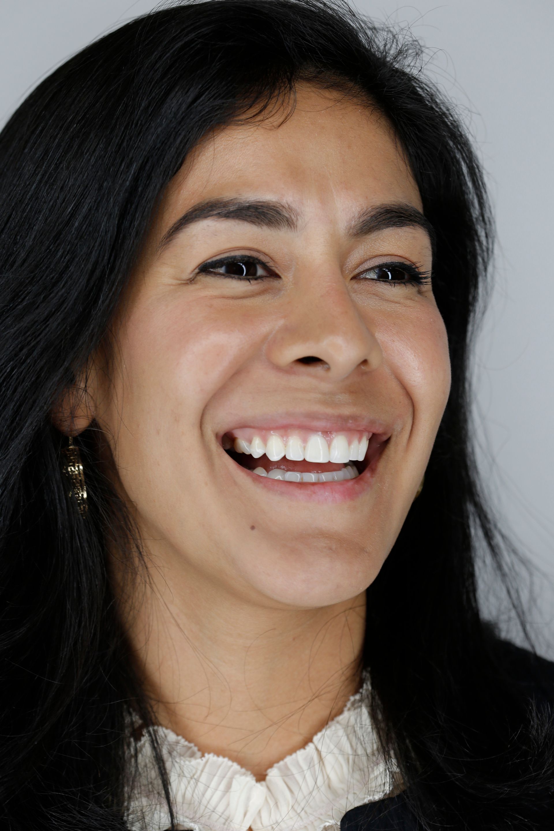 Smiling woman with dark hair in a white blouse against a gray background