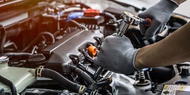 A man is working on a car engine with a wrench.