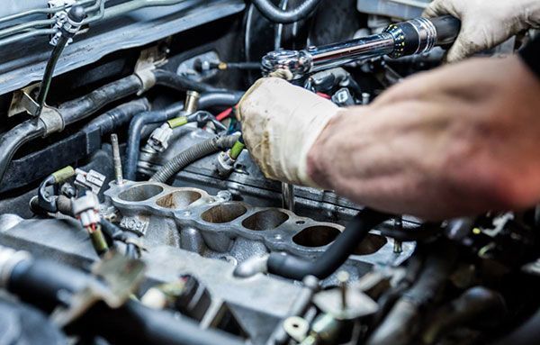 A man is working on a car engine with a wrench.