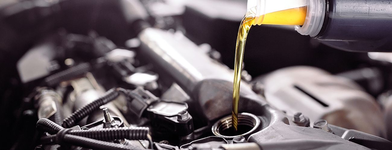 Golden engine oil is being poured from a plastic bottle into the oil filler cap of a car engine.