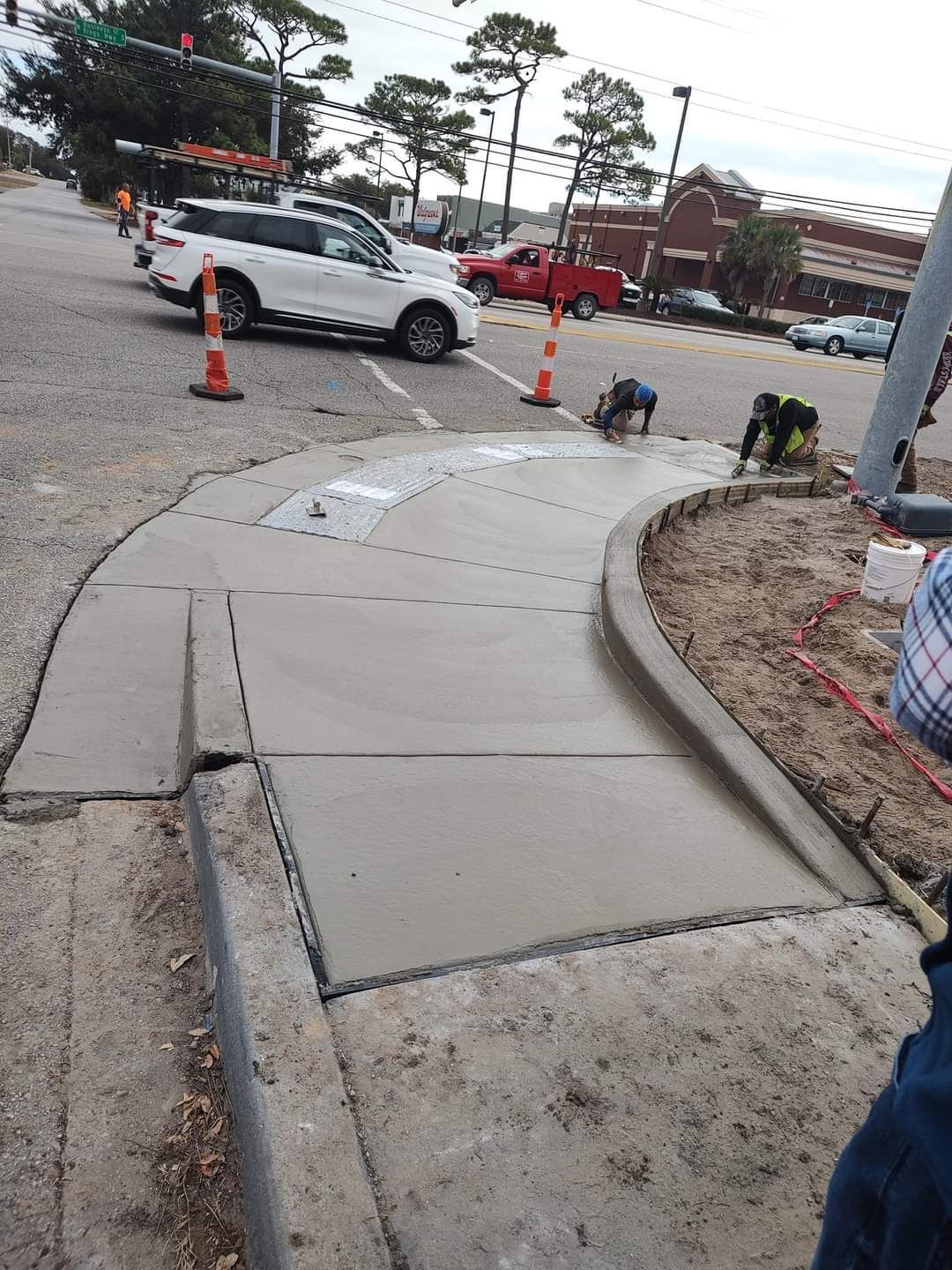 Damaged sidewalk ramp with cracked concrete near a parking lot and traffic cones beside a white SUV