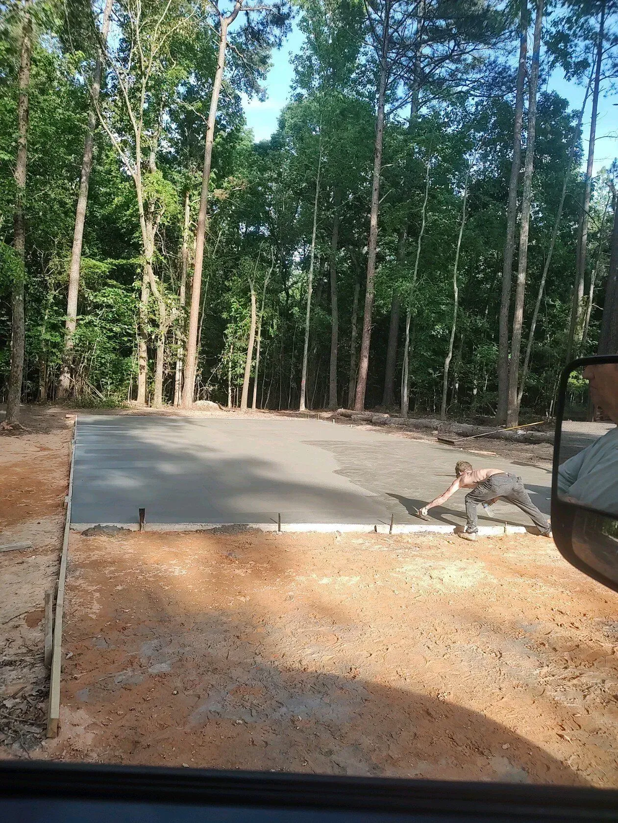 Concrete slab in a wooded area, with gravel foreground and a parked vehicle edge at right.