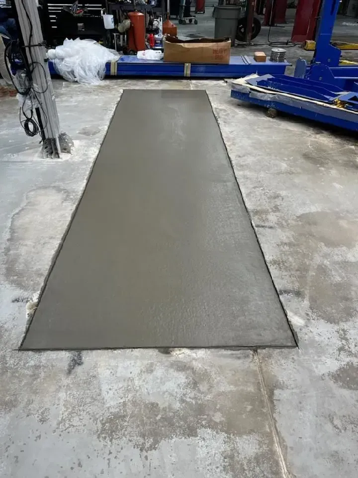 Fresh gray concrete ramp or walkway in an industrial workshop, with equipment and tools in the background.