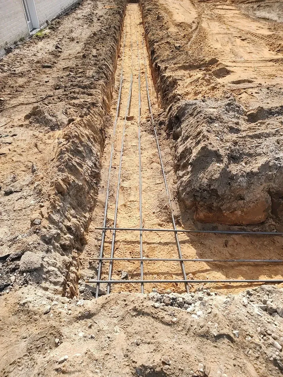 Shallow trench with exposed rebar on muddy construction site