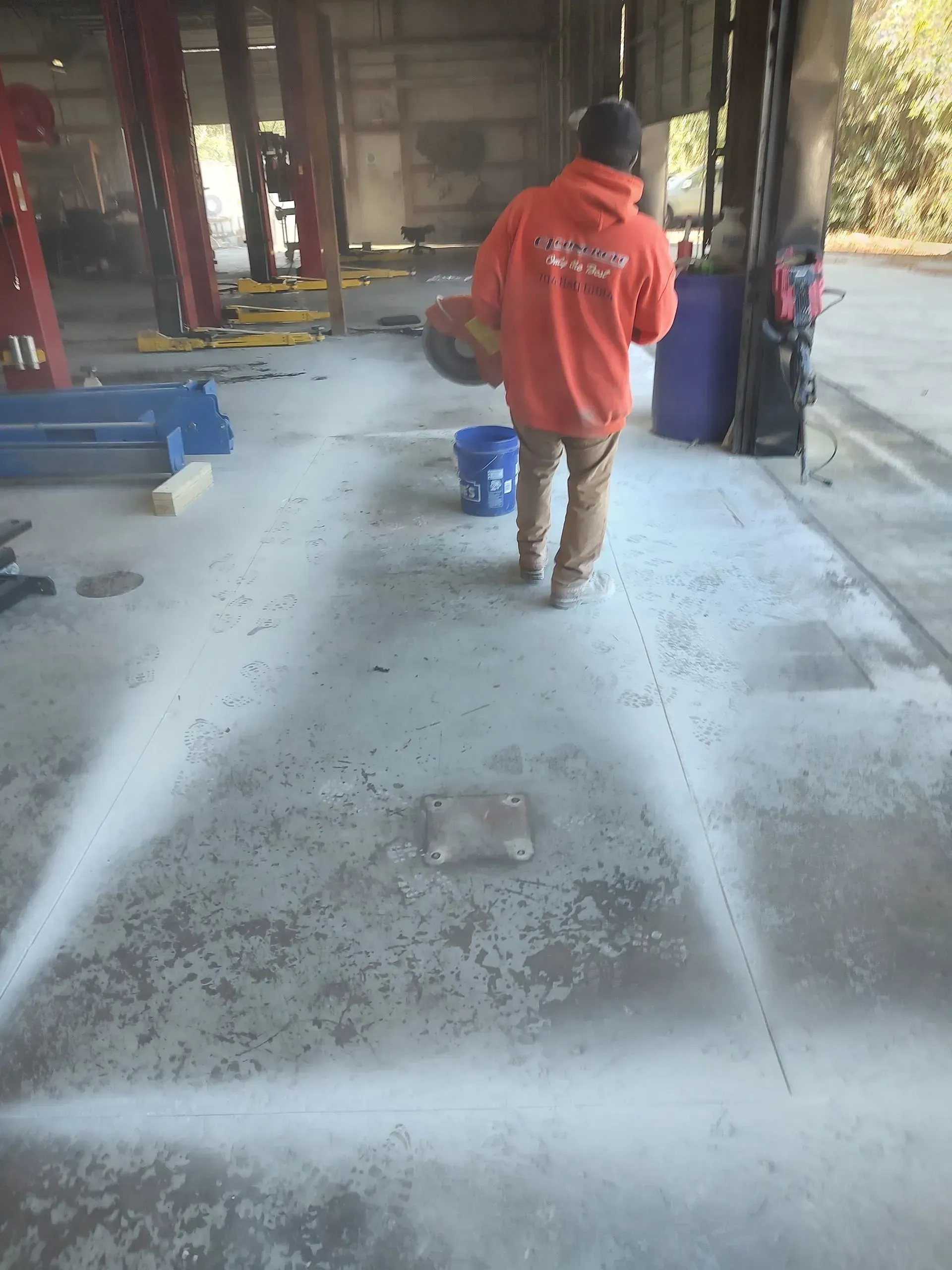 Person in an orange jacket walks across a wet concrete floor in an industrial space.