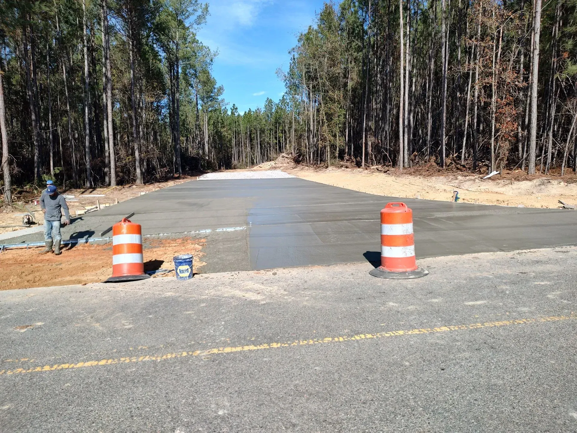 Newly paved road blocked by orange traffic barrels in a wooded area