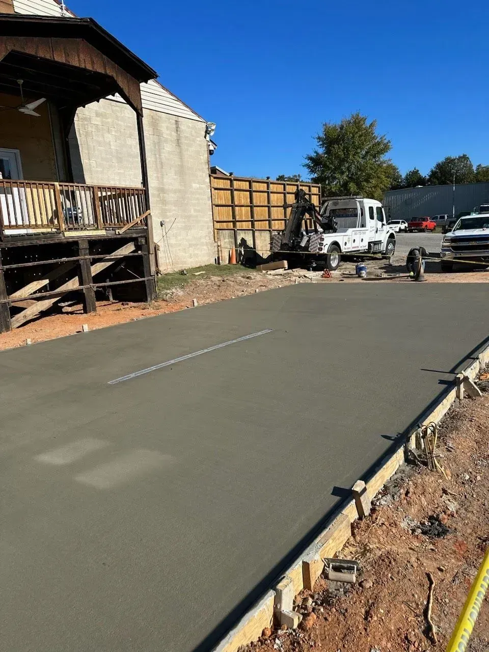 Freshly poured concrete driveway beside a house, with parked work trucks and a wooden fence ahead