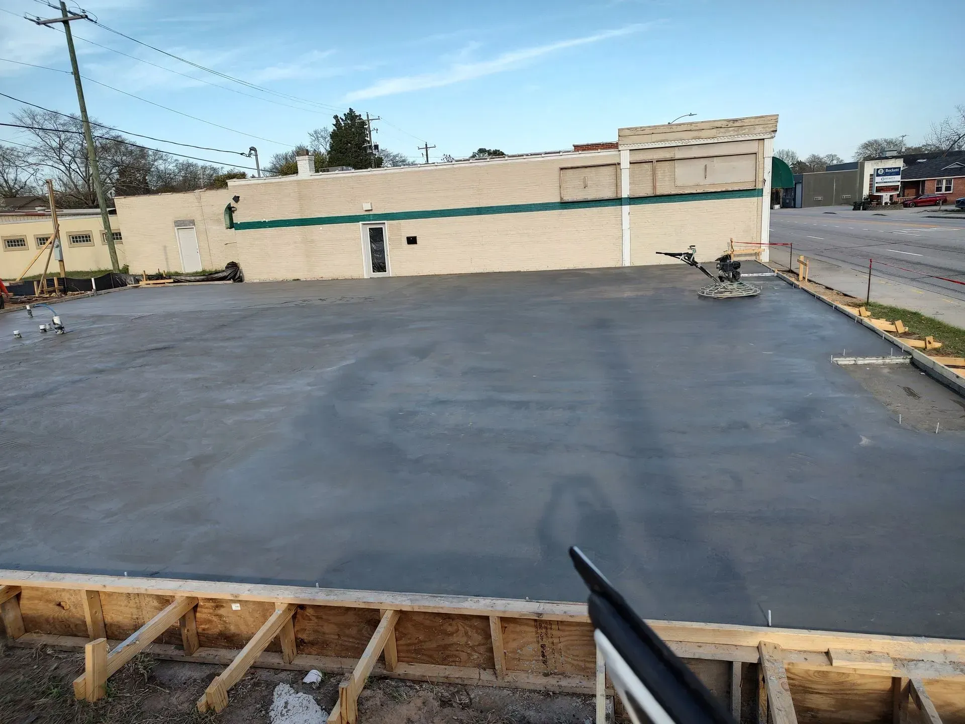 Flat rooftop under construction with fresh dark roofing and a beige wall in the background.