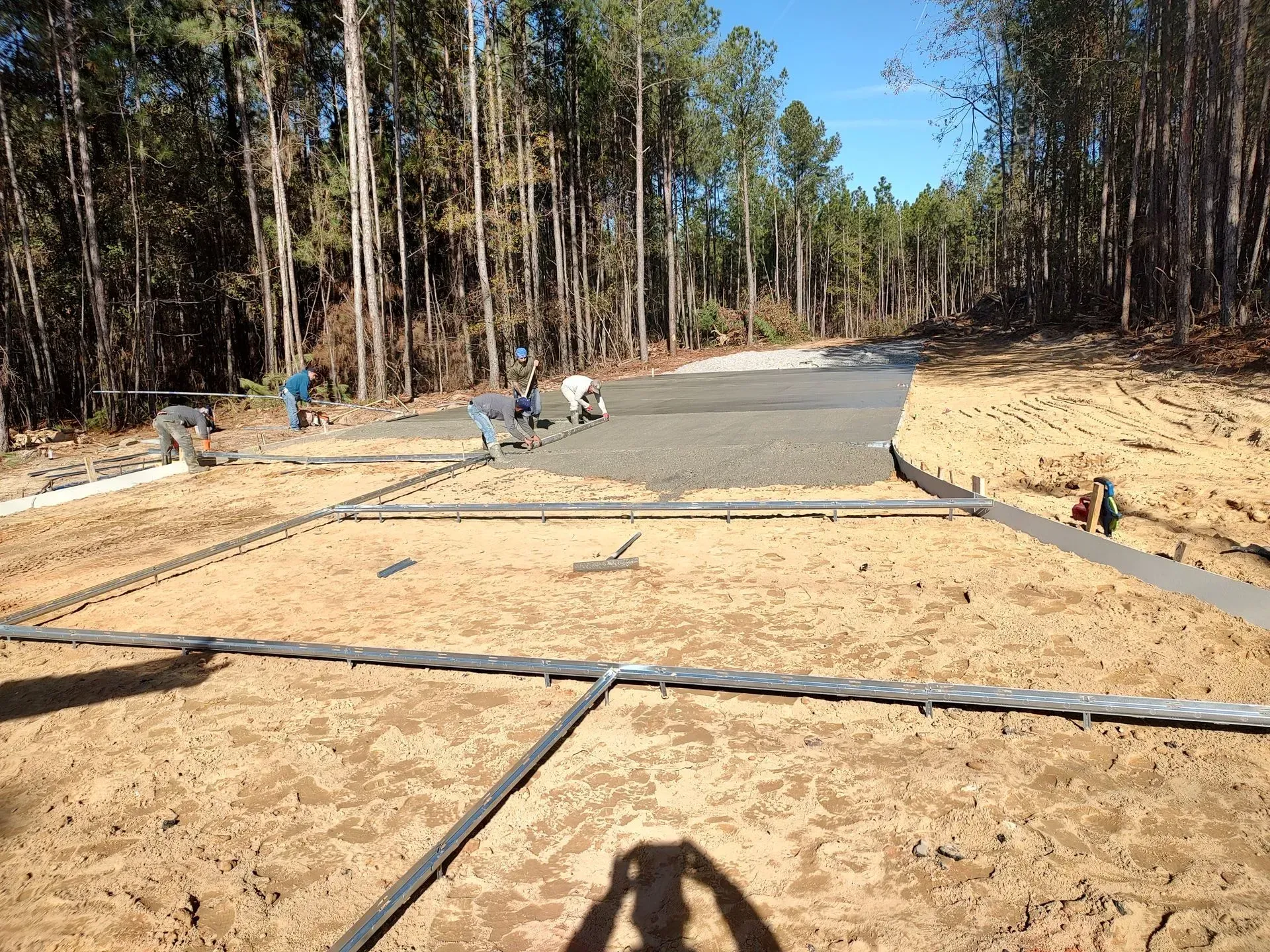 Workers pouring a concrete path through a wooded area, with forms and rails in place