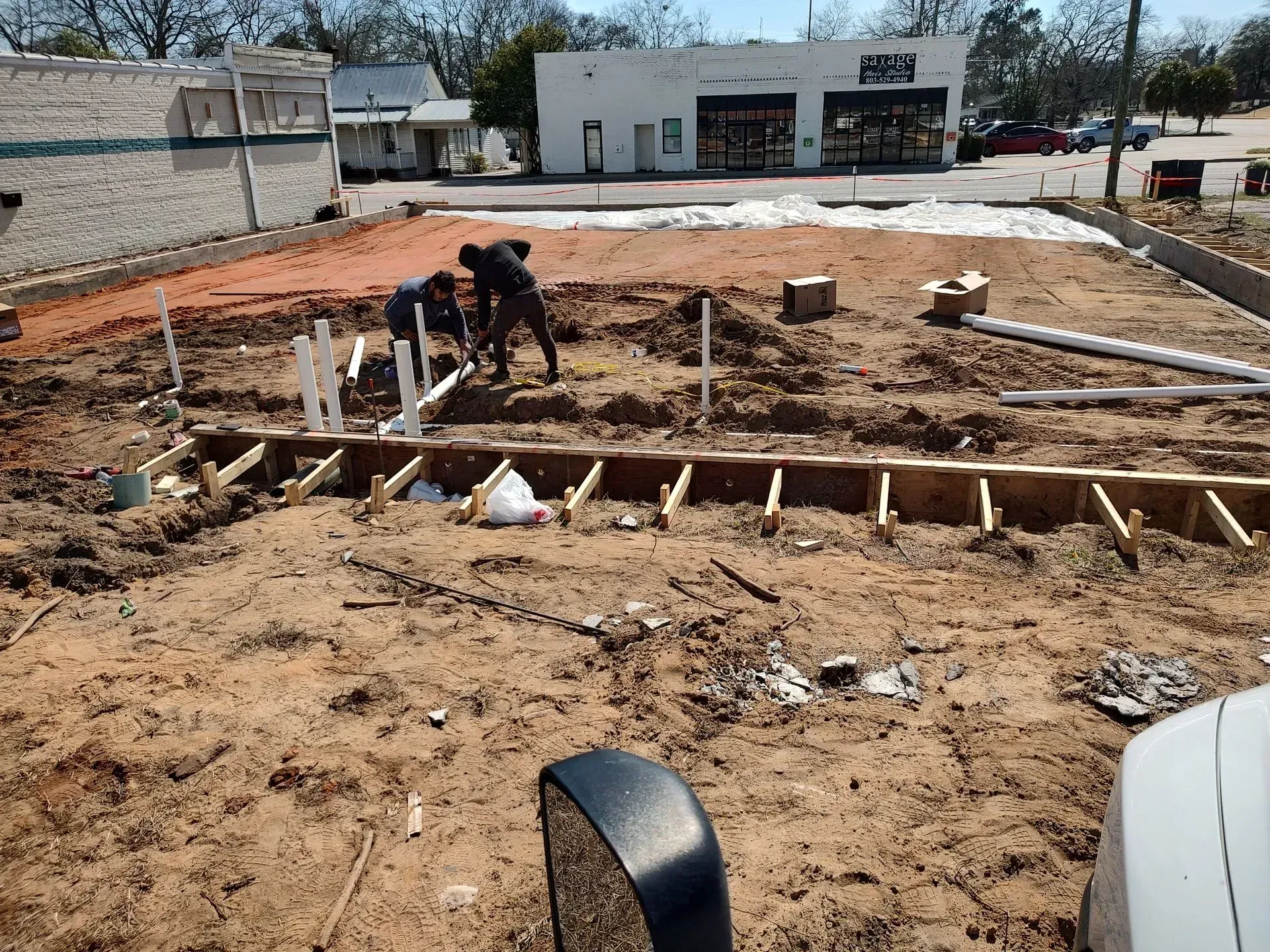 Workers at a construction site digging a large foundation pit beside a building.