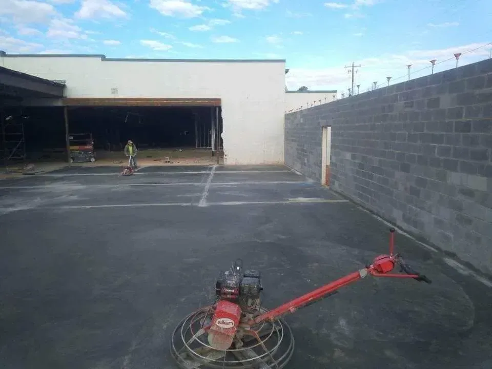 Industrial lot with an open garage, concrete wall, and a red floor grinder in the foreground.