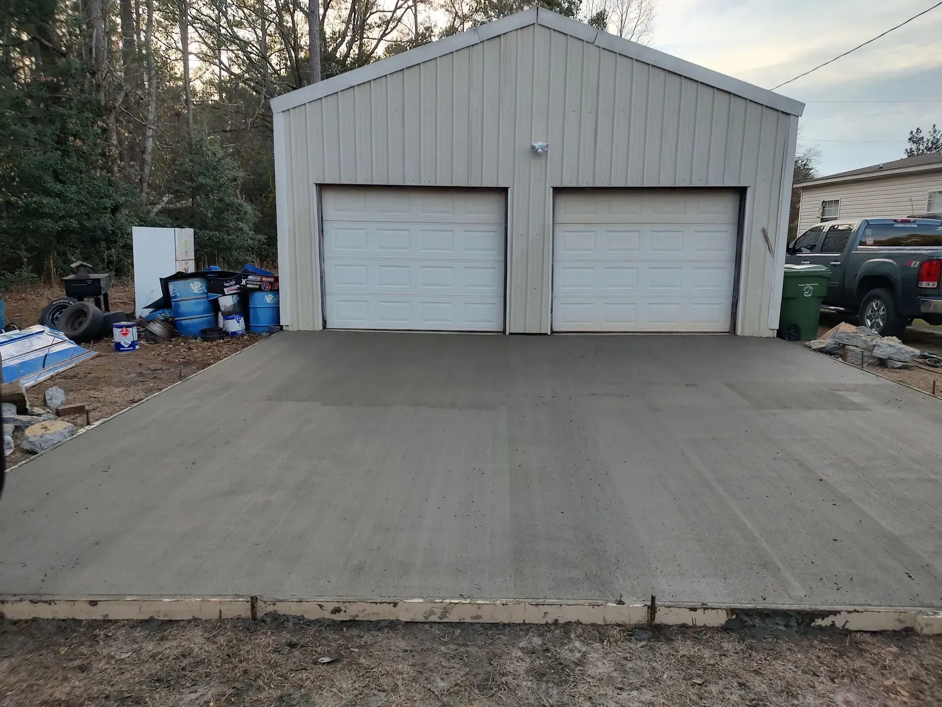 Concrete driveway leading to a white two-car garage with a gray metal roof and trees behind it