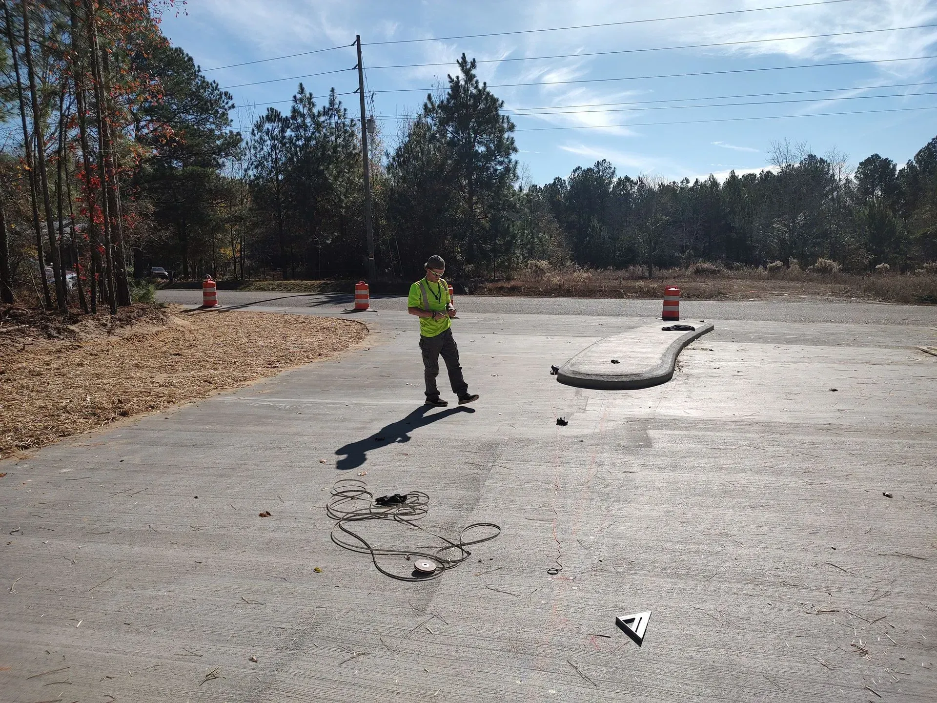 Worker in a neon vest standing on a concrete road with traffic cones and damaged pavement under a clear sky