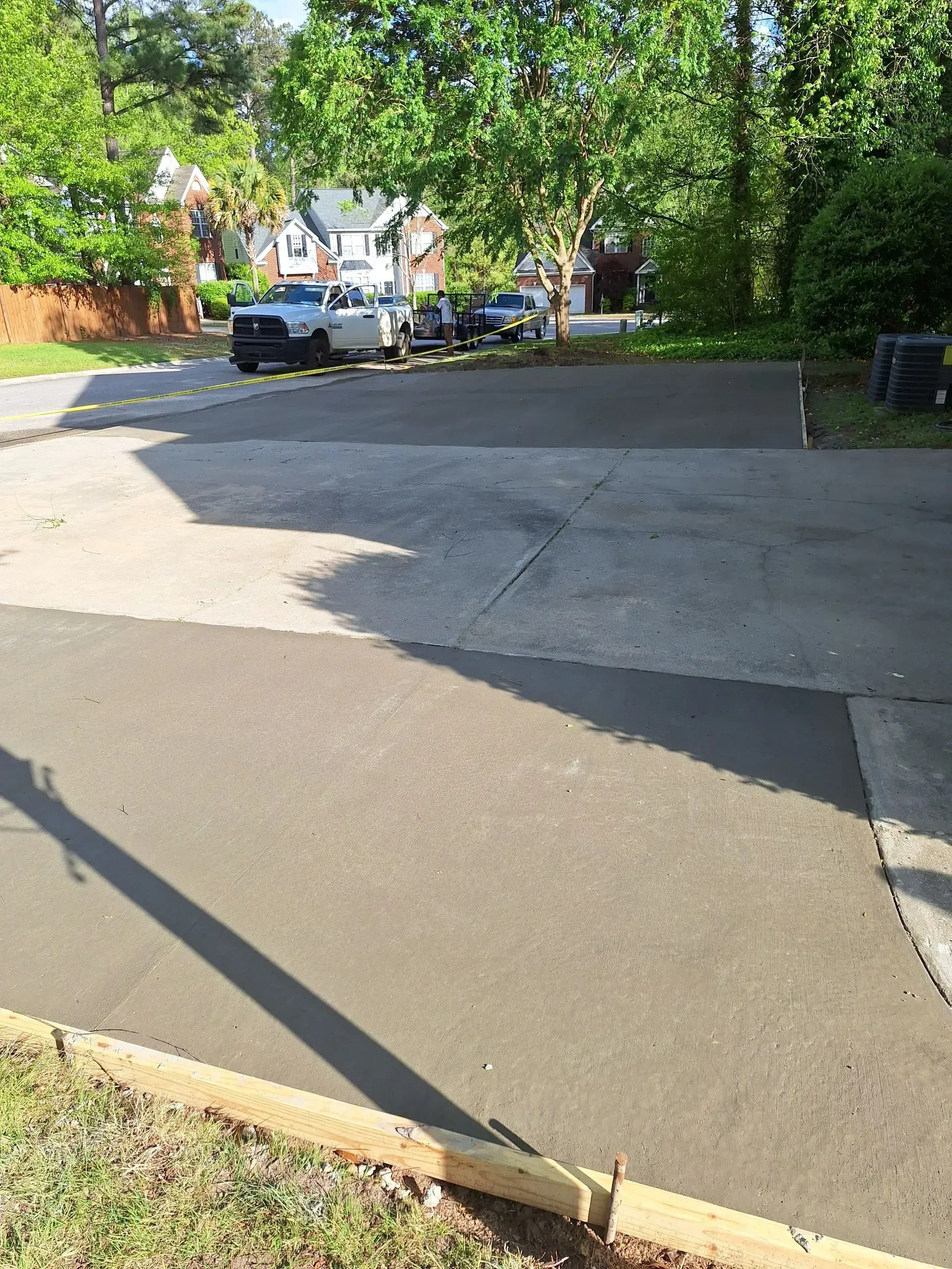 Quiet residential street with parked cars, trees, and a paved driveway in bright sunlight