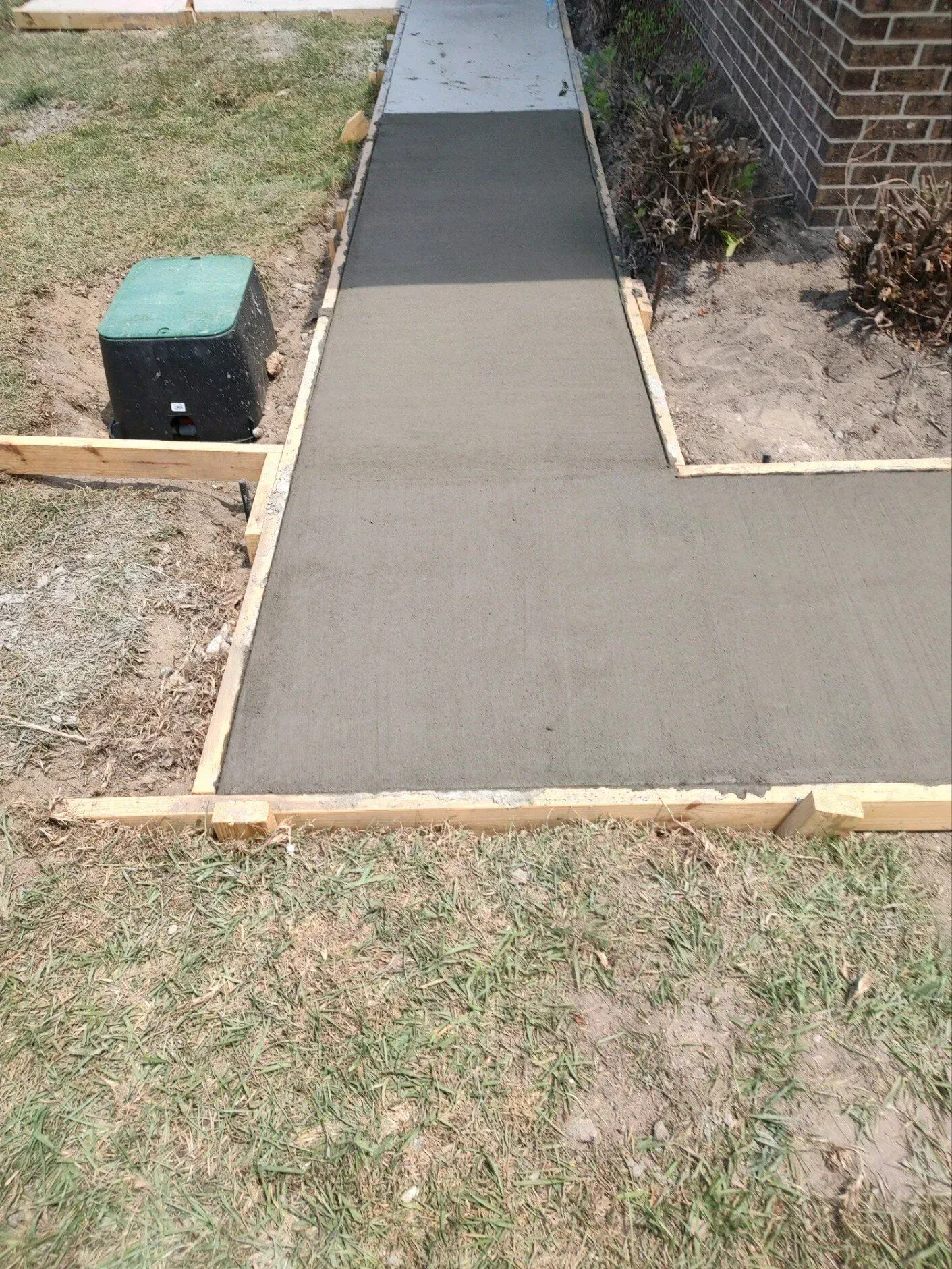 New concrete walkway under construction beside a house, with wooden forms and a grassy yard.