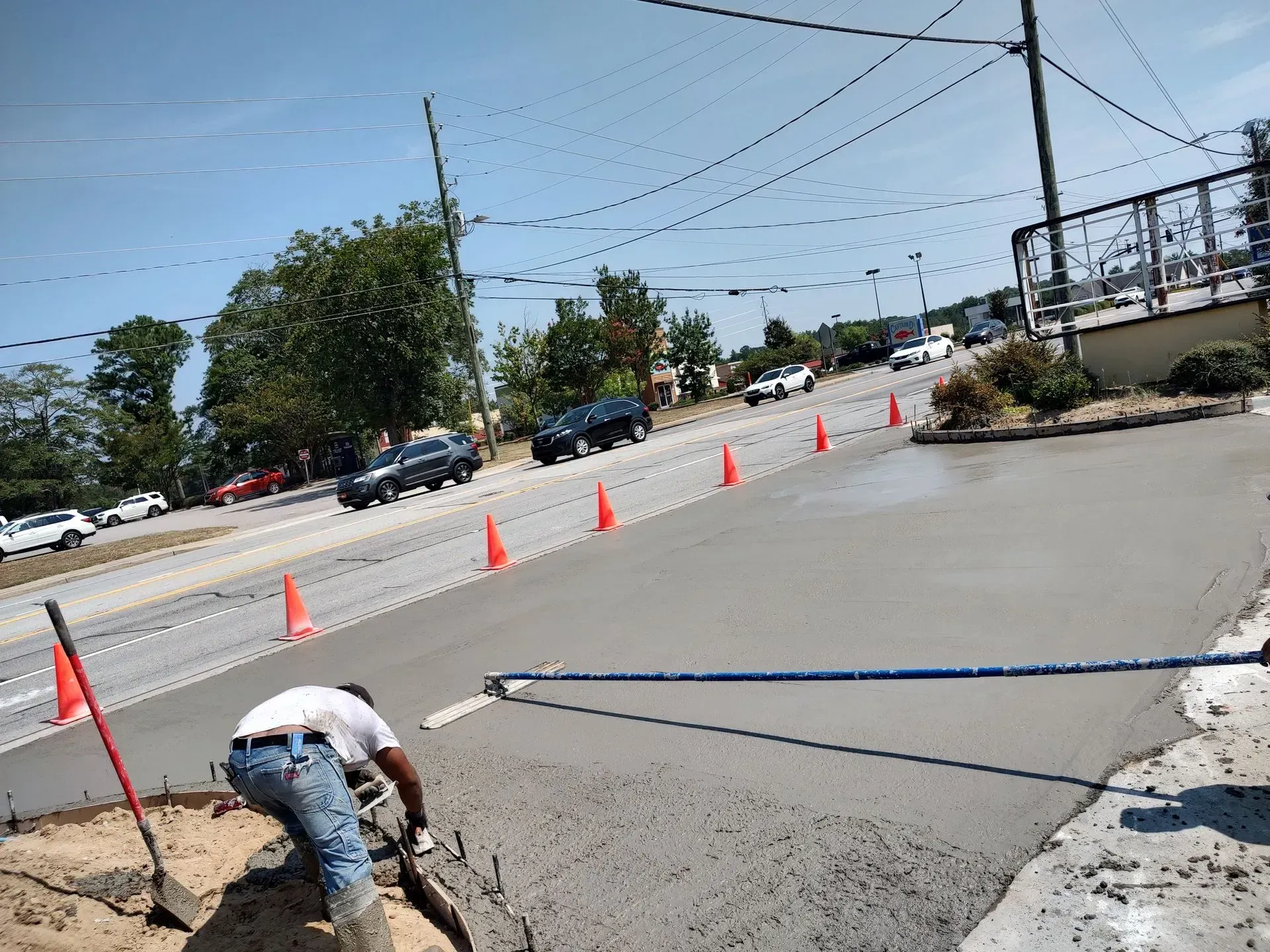 Worker laying asphalt near orange cones at a roadside construction site.