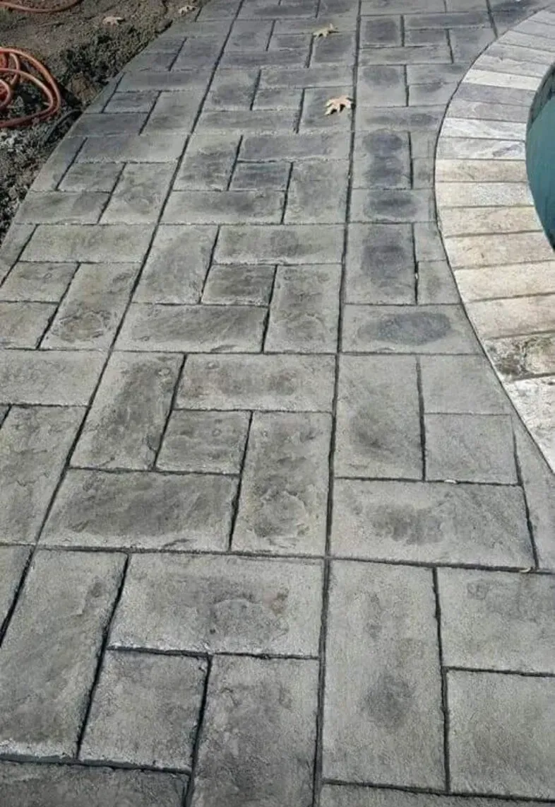 Curved gray stamped-concrete pool deck beside blue water and stone edging