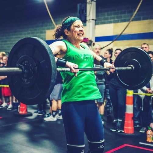A woman in a green tank top is lifting a barbell