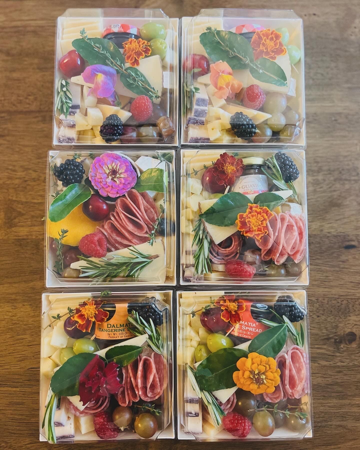 Six boxes filled with different types of food are sitting on a wooden table.