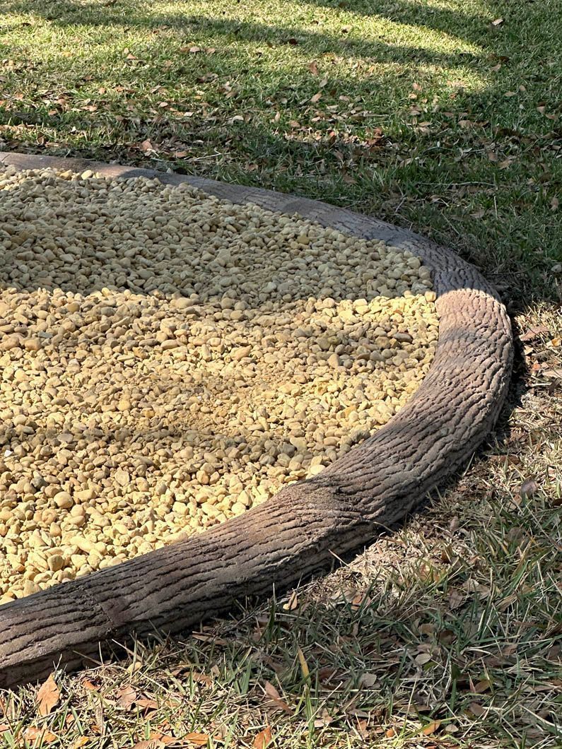Curved concrete border resembling wood separates gravel and grass.