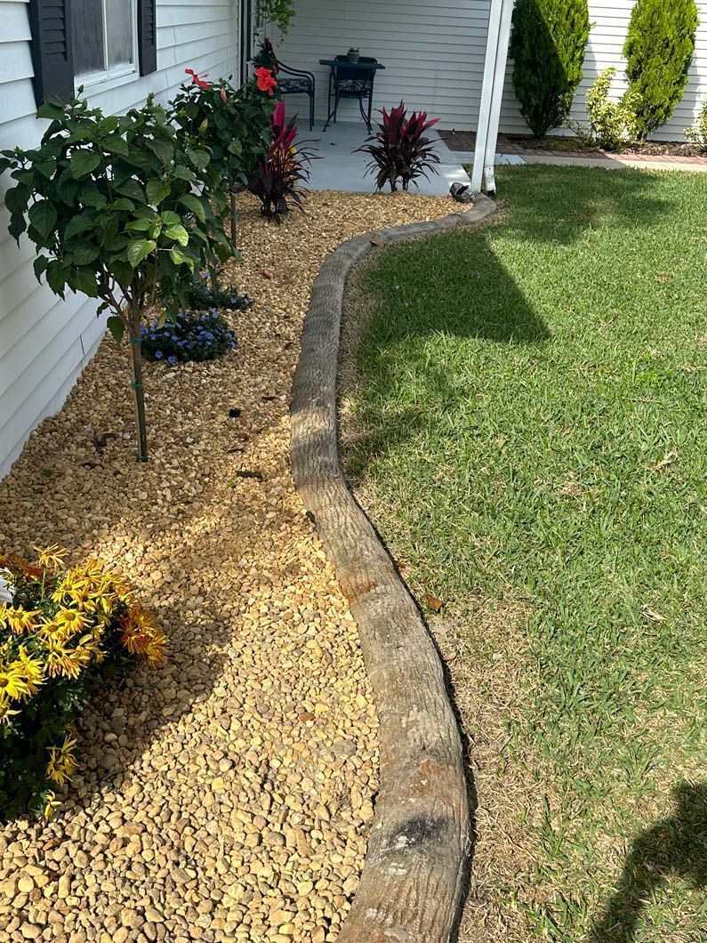 Yard with a concrete border, brown mulch, green grass, and plants with flowers.