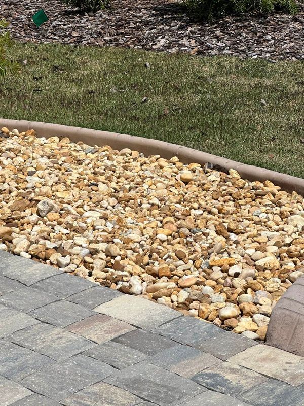 Stone walkway borders a bed of tan river rocks and a strip of green grass.