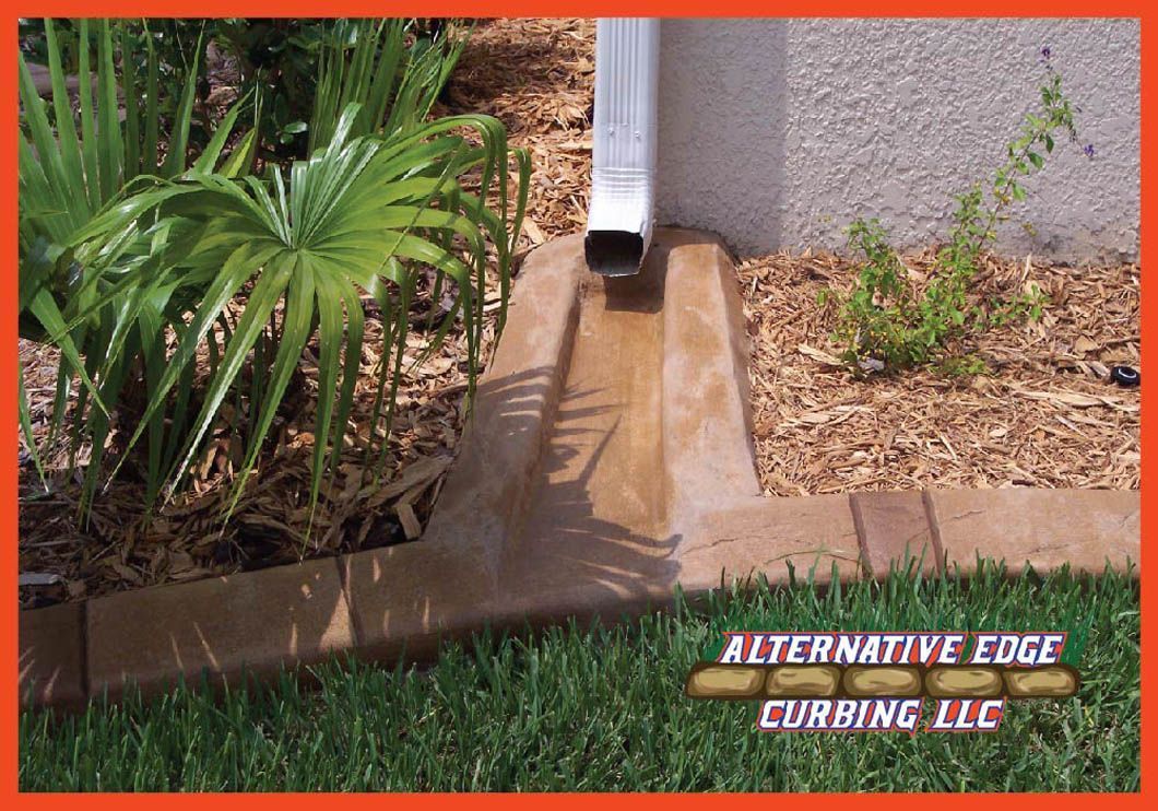 Concrete curb with a channel under a downspout, channeling water to a bed of mulch.