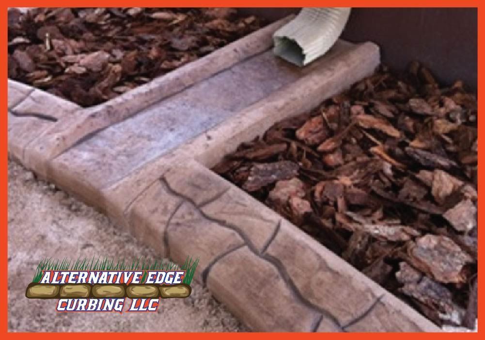 Concrete landscape edging with a built-in drainage channel, bark mulch, and a downspout.