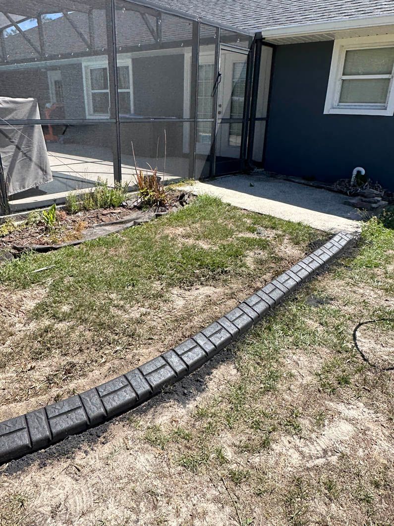 Black brick-like edging borders a grassy area alongside a dark blue building and screened patio.