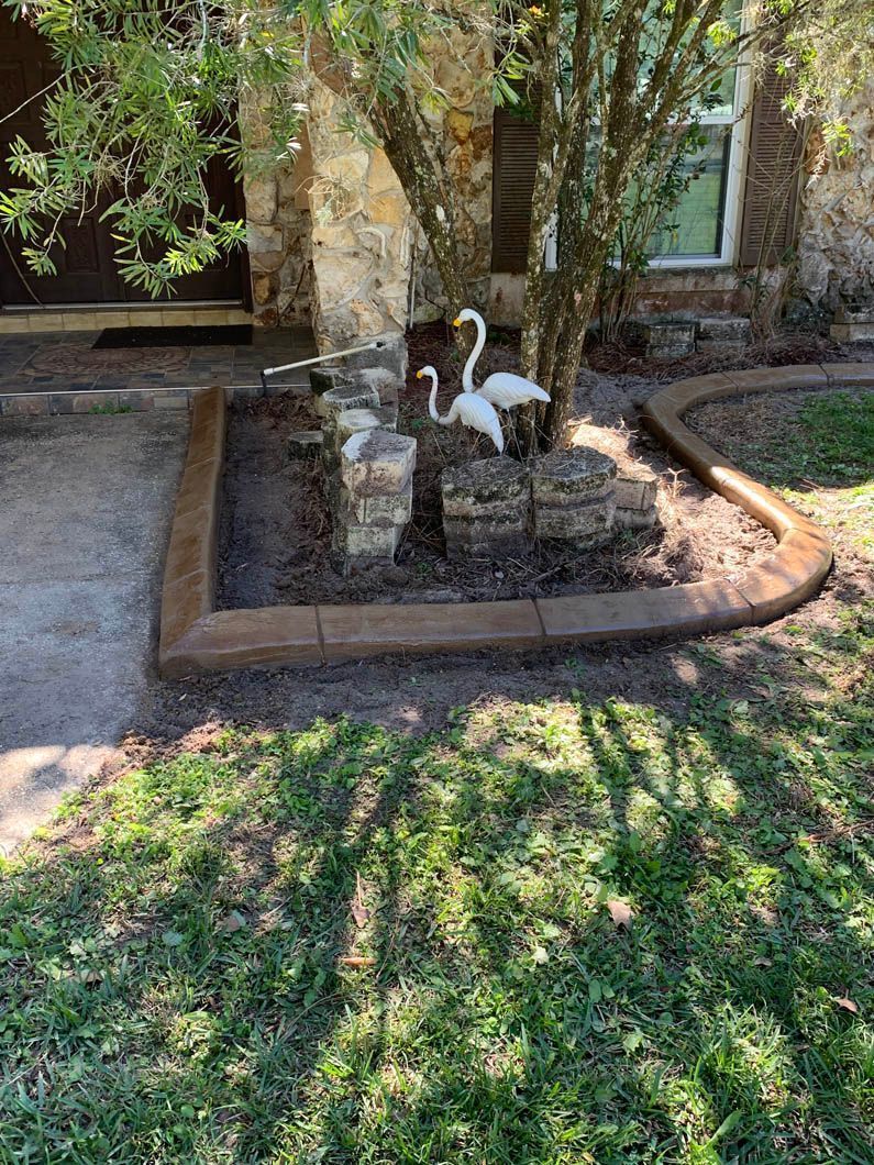 Brown concrete curbing around a tree and stone structure with two swan statues in front of a stone house.