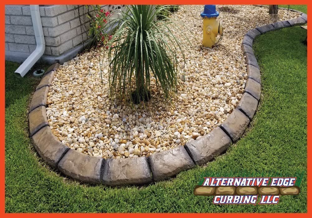 Concrete curbing borders a landscaped bed of rocks and greenery.