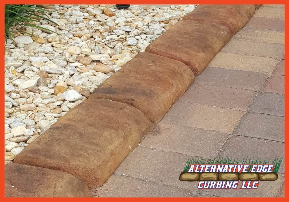 Brown, textured curbing separates a paved walkway from gravel.