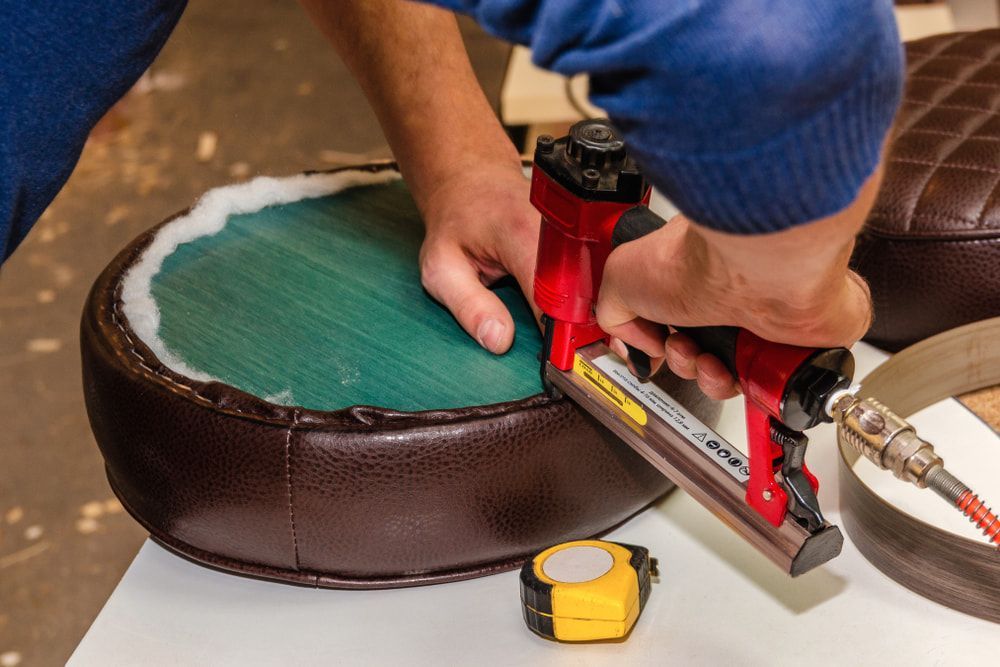 A Person Is Using A Stapler On A Chair Seat — Coastal Upholstery In Berkeley Vale, NSW
