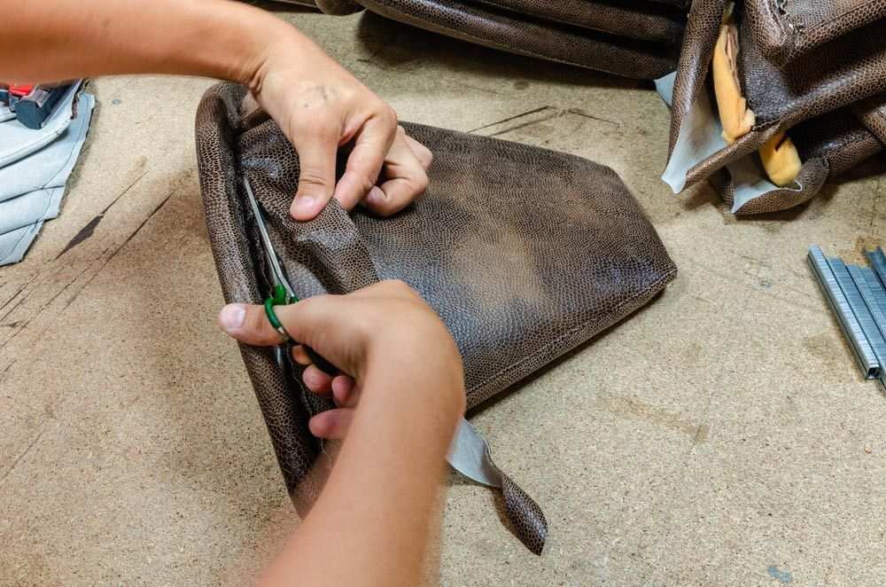 A Person Is Cutting A Piece Of Leather With Scissors — Coastal Upholstery In Berkeley Vale, NSW