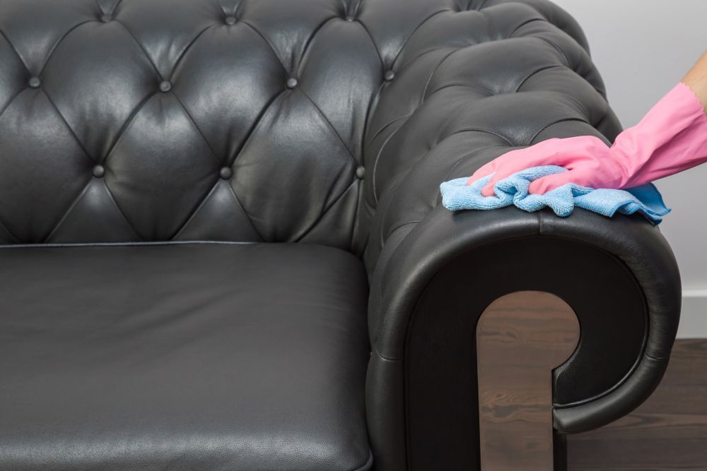 A Person Wearing Pink Gloves Is Cleaning A Black Leather Couch— Coastal Upholstery In Berkeley Vale, NSW