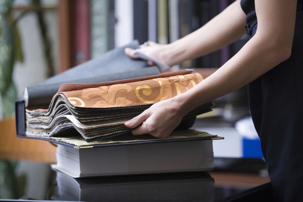 A Woman Is Holding A Stack Of Fabric Samples On A Table — Coastal Upholstery In Berkeley Vale, NSW