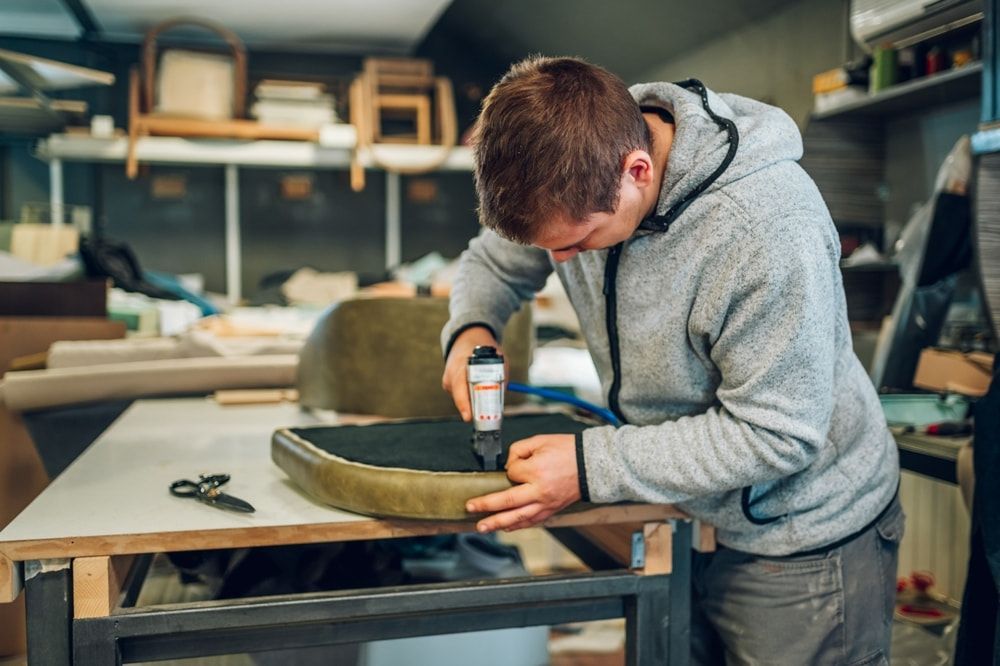 A Man Is Working On A Chair In A Workshop — Coastal Upholstery In Berkeley Vale, NSW