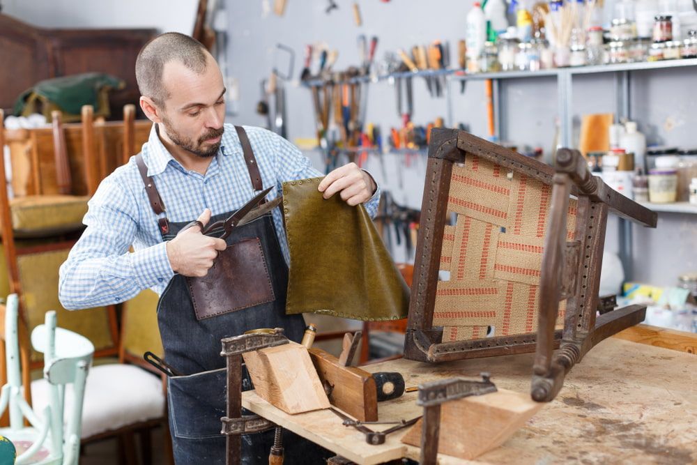 A Man Is Working On A Chair In A Workshop — Coastal Upholstery In Berkeley Vale, NSW