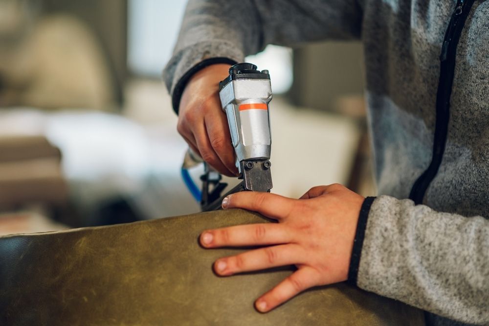 A Person Is Using An Air Stapler To Staple A Piece Of Fabric — Coastal Upholstery In Berkeley Vale, NSW