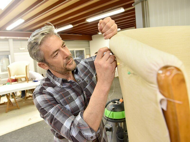 A Man Is Working On A Couch In A Factory — Coastal Upholstery In Berkeley Vale, NSW